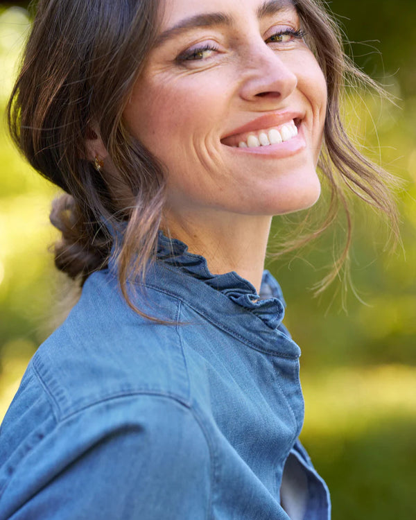 Woman wearing Woman wearing Frank & Eileen Eileen Ruffle in Vintage Stonewashed Indigo with a blurred green background