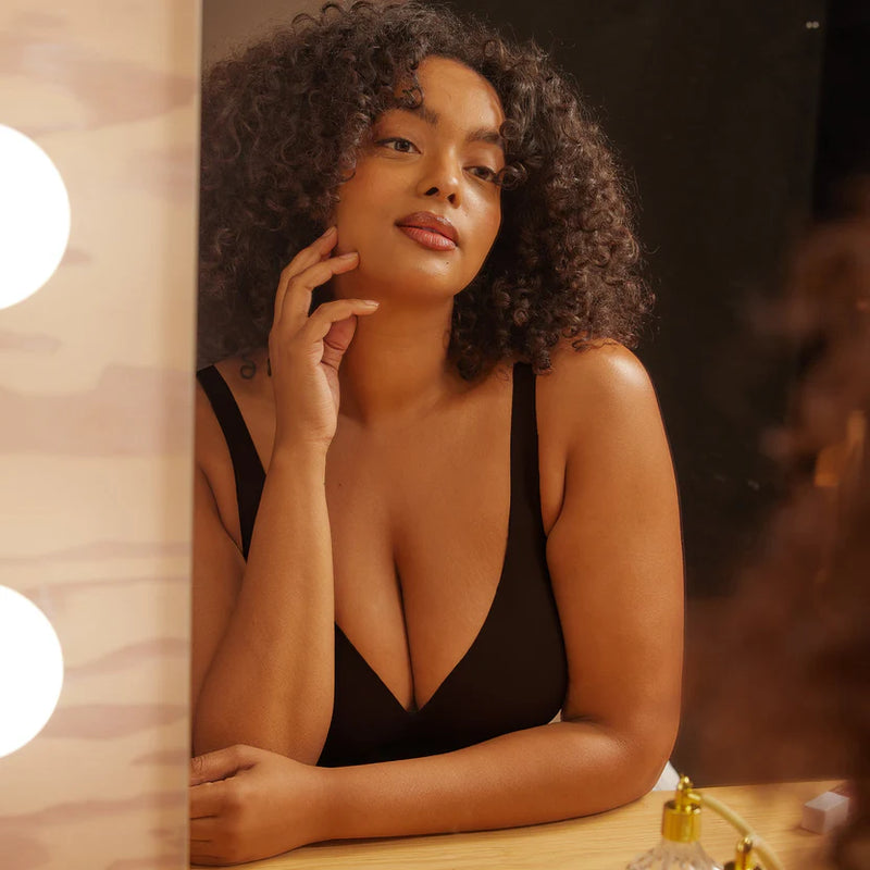 woman looking in mirror wearing Evelyn & Bobbie Starlette Plunge Bra in Black white background