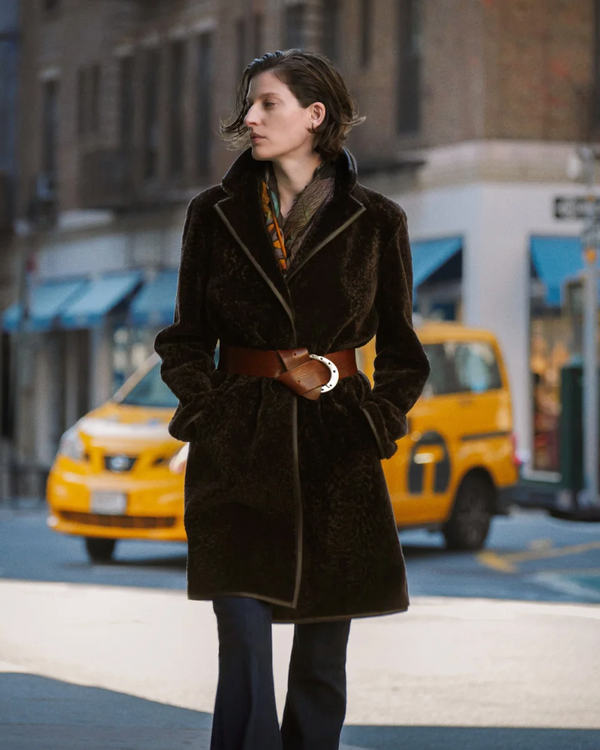 woman wearing Grenn Pilot Amari Car Coat in chocolate in a city with a blurred taxi cab in the background